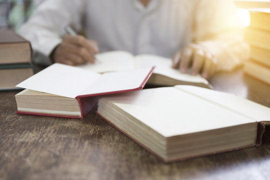 man reading book with textbook stack on wooden desk