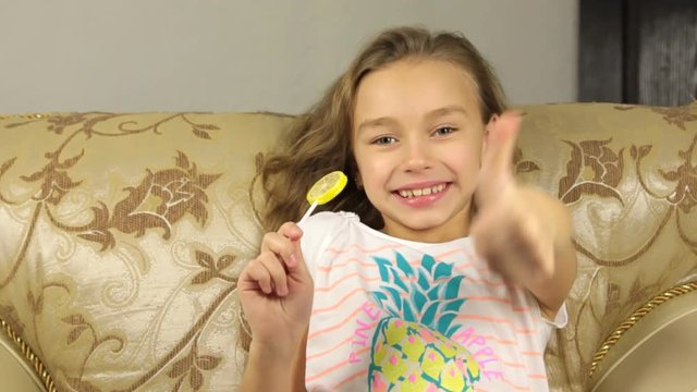 Girl licking candy on a stick in the form of lemon and raises the thumbs up.