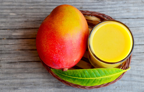 Fresh mango smoothie,ripe mango fruit and mango tree leaf in a small basket on old wooden background.Healthy food,diet or vegan food concept.Top view.