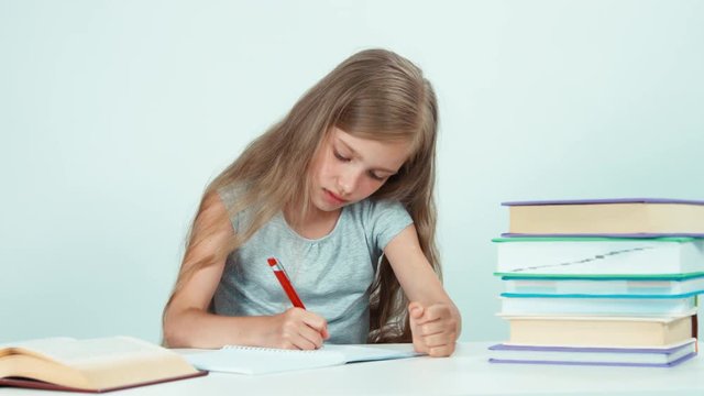 Close up portrait schoolgirl something writing in her school notebook on white background. Child girl sitting at the desk