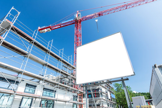 Leeres Schild auf Baustelle f&uuml;r modernen Neubau mit Ger&uuml;st und Kran im Hintergrund