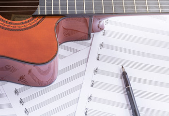 Acoustic guitar, sheet music and fountain pen on wooden table