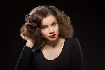 Beautiful lady with modern hairstyle posing isolated on black background. Pretty woman in black dress touching her gorgeous hair.