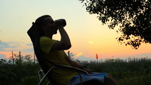 Silhouette of young man sitting on sunset or sunrise. Confident teenage boy thinking on cliff stone. Hope. Sadness. Freedom.