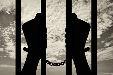 Silhouette of human hands in handcuffs behind bars