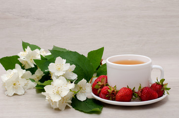 Flowers of jasmine, white mug with tea, strawberries, close-up
