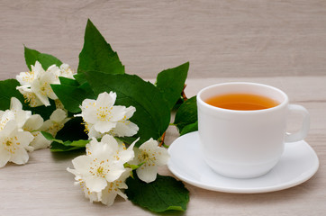 White mug with tea and a branch of jasmine on a wooden background, close-up