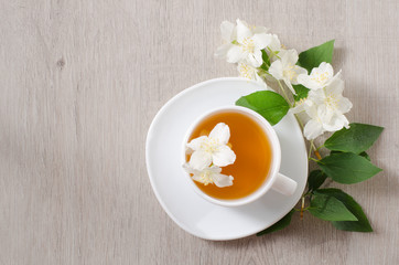 Top view of a mug of herbal tea and jasmine flowers on a wooden table, space for text