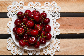 Red cherries on a lacy napkin on wooden background, a top view