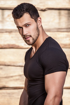 Portrait of young beautiful sporty man in t-shirt against wooden wall.