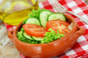 Fresh green salad consisting of lettuce, tomatoes and cucumbers in clay bowl on checkered cloth
