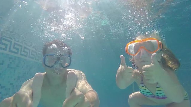 father and daughter in swimming masks under water raised thumbs up