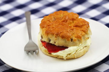English scone with raisins with traditional clotted cream and strawberry jam on white plate
