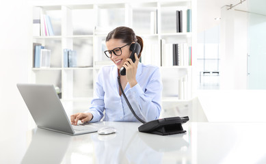 smiling woman in office at desk with computer, talking on the ph