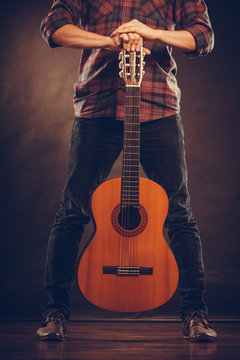 Guitarist is standing with wooden guitar.