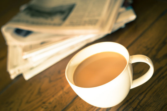 Vintage toned image of Cup of coffee on table with newspaper in the background.