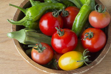 Fototapeta na wymiar 木製のボウルに入ったトマト、オクラ、獅子唐辛子などの夏野菜