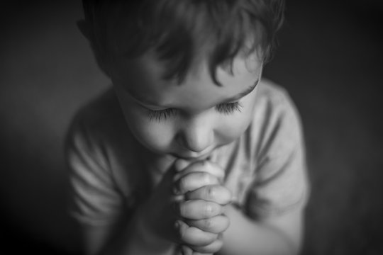Cute Young Boy Praying in Black and White / A cute young boy praying with hands clasped, in black and white.