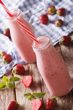 Cold strawberries milkshake in glass bottles close-up on the table. vertical
