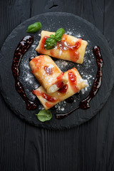 Above view of stuffed rolled crepes on a black wooden background