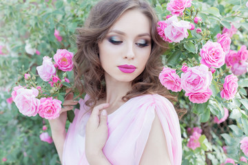 Fototapeta premium beautiful sexy girl in a pink dress standing in the garden roses in a sunny bright summer day with a gentle make-up and bright puffy big lips