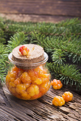 Cloudberry jam in glass jar on wooden background