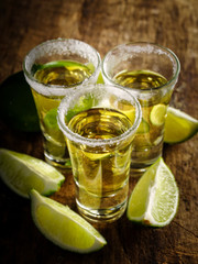 Gold tequila shot with lime on wooden background, selective focus.