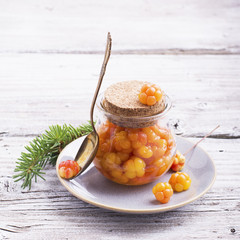 Cloudberry jam in glass jar on wooden background