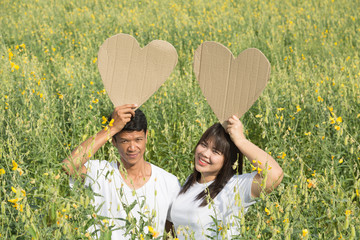 asian couple holding heart symbol in yellow field at summer time