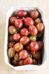 Frische Stachelbeeren in einem Karton stehen auf einem Holzbrett