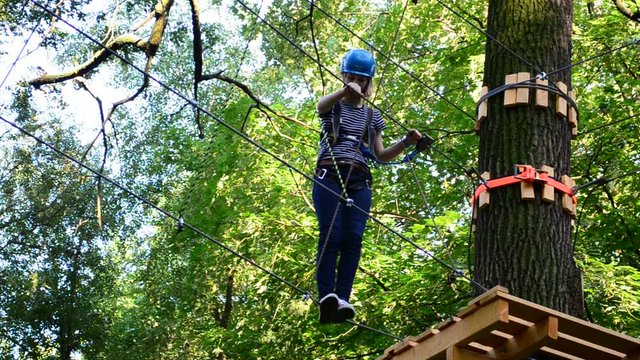 The girl the teenager overcomes obstacles between trees at height. Rope town.