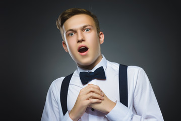 Closeup Portrait of handsome boy with astonished expression while standing against grey background