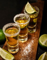 Mexican Gold Tequila with lime and salt on wooden table, selective focus.