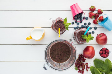 smoothie in mason`s jars, mint leaf,  colorful baby buckets, berries, apples, redcurrant, spinach, bowl of a blender with drink, top view