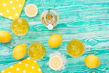 lemonade or limoncello in glasses with ice cubes, sherbet glass with ice cubes, bottle with drink, lemon fruits on turquoise colored wooden table decorated with yellow napkins at polka dots top view - 115996866