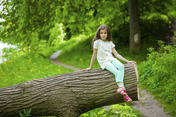 Little Girl in white dress sitting on tree trunk over green gras
