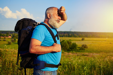 Side view of aged man with rucksack in the field wiping his fore