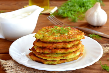 Squash delicious fried pancake with dill. Fried golden pancakes with zucchini and dill. Make delicious zucchini dishes. Cheap and easy meal idea. Sauce, garlic, fork, olive oil, dill on a wooden table