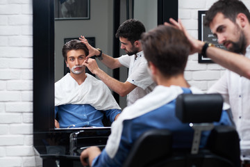 The barber shaves beard with razor and foam
