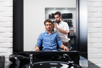 Fototapeta na wymiar hairstylist is combing carefully the client's hair in barbershop