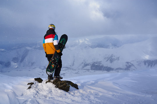 Snowboarder standing  a rock on  edge  cliff