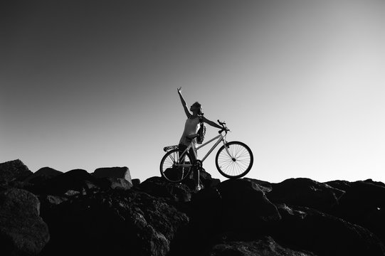 Young woman with backpack standing on the shore near his bike an