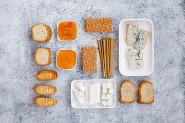 Set of four cheeses with crispbread, crackers and jam on white marble table. Flat lay.