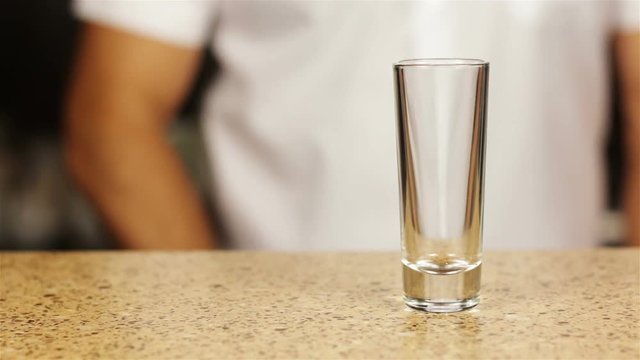 Barman pouring whiskey into three shot glasses with ice