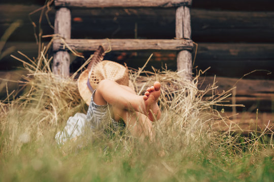 Barefoot boy sleeps on the grass near ladder in haystack