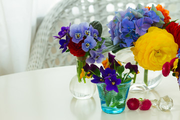 Set of colorful freshly cut flowers in glass vases on white desktop