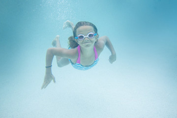 Cute smiling little girl swimming underwater in an outdoor swimming pool