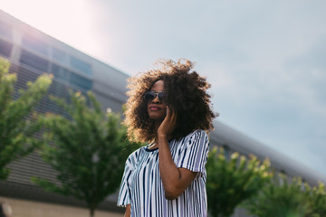 Close-up portrait of a happy african american woman in sunglasses walking outdoors with mobile phone