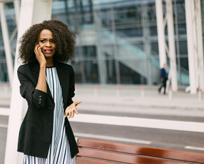 Worried young African American businesswoman talking on phone, modern building as background