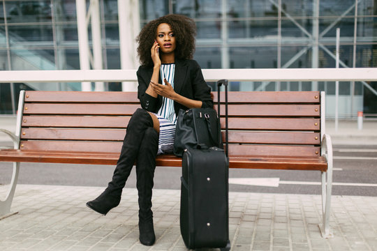 Confident African American businesswoman using cell phone in airport with her suitcase